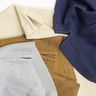 Top-down view of folded polo shirts in muted shades of navy, beige, olive, and grey, showcasing textile quality, color choices, and fabric texture diversity.
