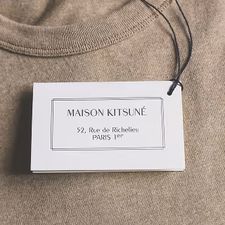 Close-up of a beige sweater displaying a stylish and minimalistic branded tag labeled "Maison Kitsuné" from Paris, highlighting brand identity and craftsmanship.