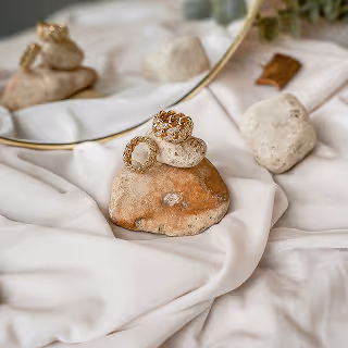 Elegant jewelry arrangement with rings positioned on stones and a soft fabric backdrop, emphasizing natural beauty and luxury.