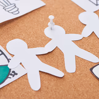 Close-up image of paper cutout figures pinned onto a corkboard, suggesting themes of teamwork, collaboration, and strategy planning.