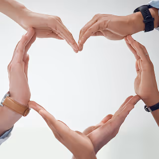 Multiple hands forming the shape of a heart together, showcasing unity, care, and teamwork on a soft white background.