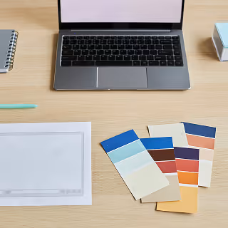 Top-down view of a workspace with a laptop, paper, color swatches, and stationery items, representing a digital design setup or mood board development.