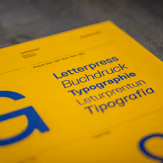 Close-up of a yellow design reference sheet with the word 'Typography' and its translations printed in blue, showcasing different fonts and letterpress terminology.