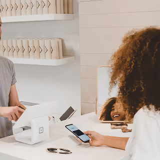 Customer making a payment using a smartphone at a minimal retail counter while the cashier smiles, demonstrating modern point-of-sale technology.