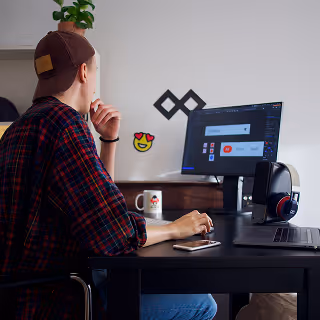 Designer working at a desk, focused on a screen displaying a branding interface, with headphones, a coffee mug, and a smartphone nearby.