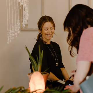 A smiling shop employee behind the counter helping a customer, with soft lighting and a natural, cozy ambiance.