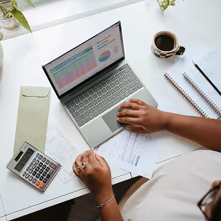 Overhead view of a person working at a white desk with a laptop, calculator, documents, and a coffee cup, representing financial planning or analysis.