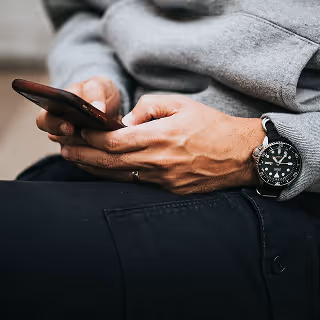 Close-up of a person in casual clothing using a smartphone with both hands, suggesting mobile business operations or social media management.