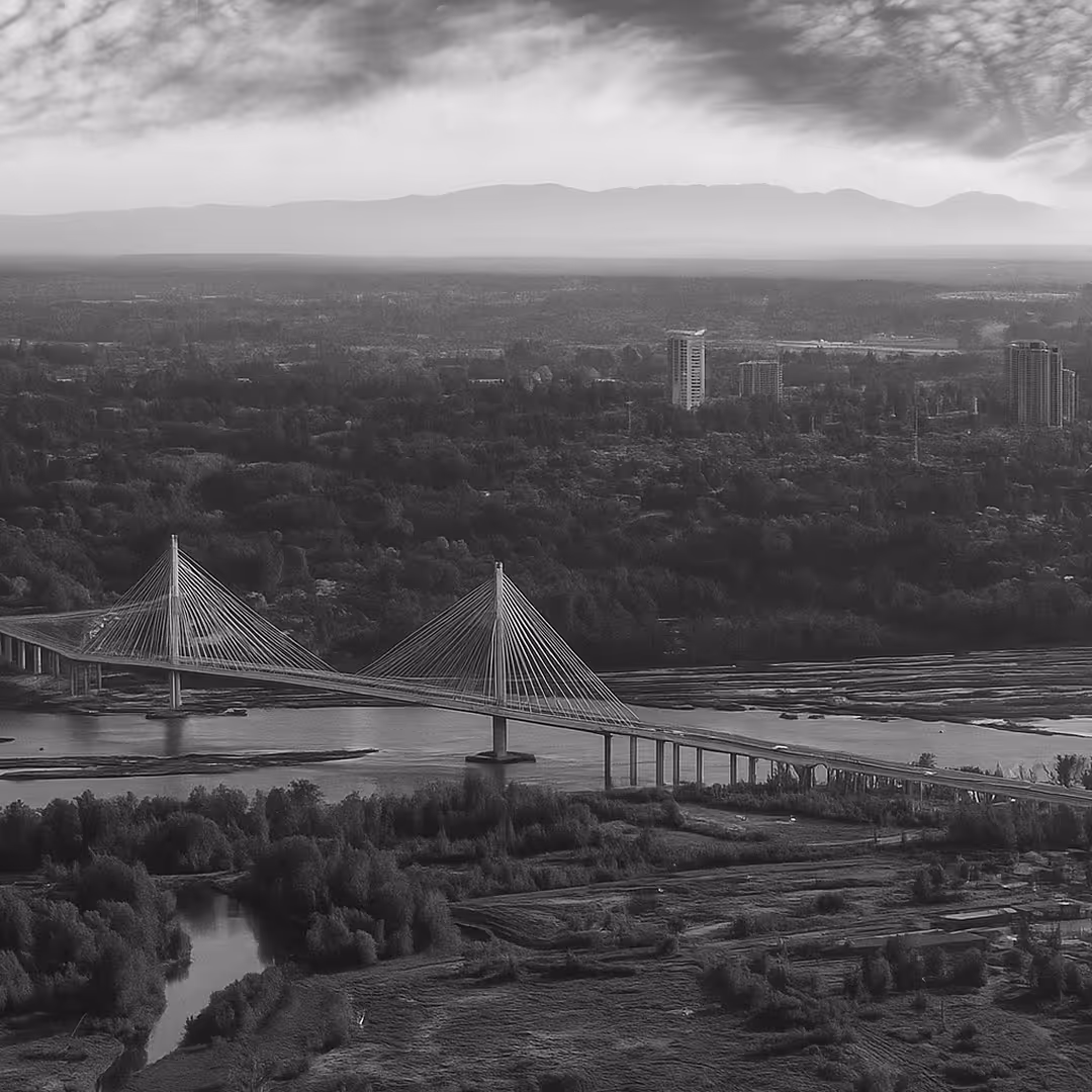 A black-and-white image of the Port Mann Bridge in British Columbia, spanning the Fraser River with cable-stayed towers, set against a dramatic cloudy sky.