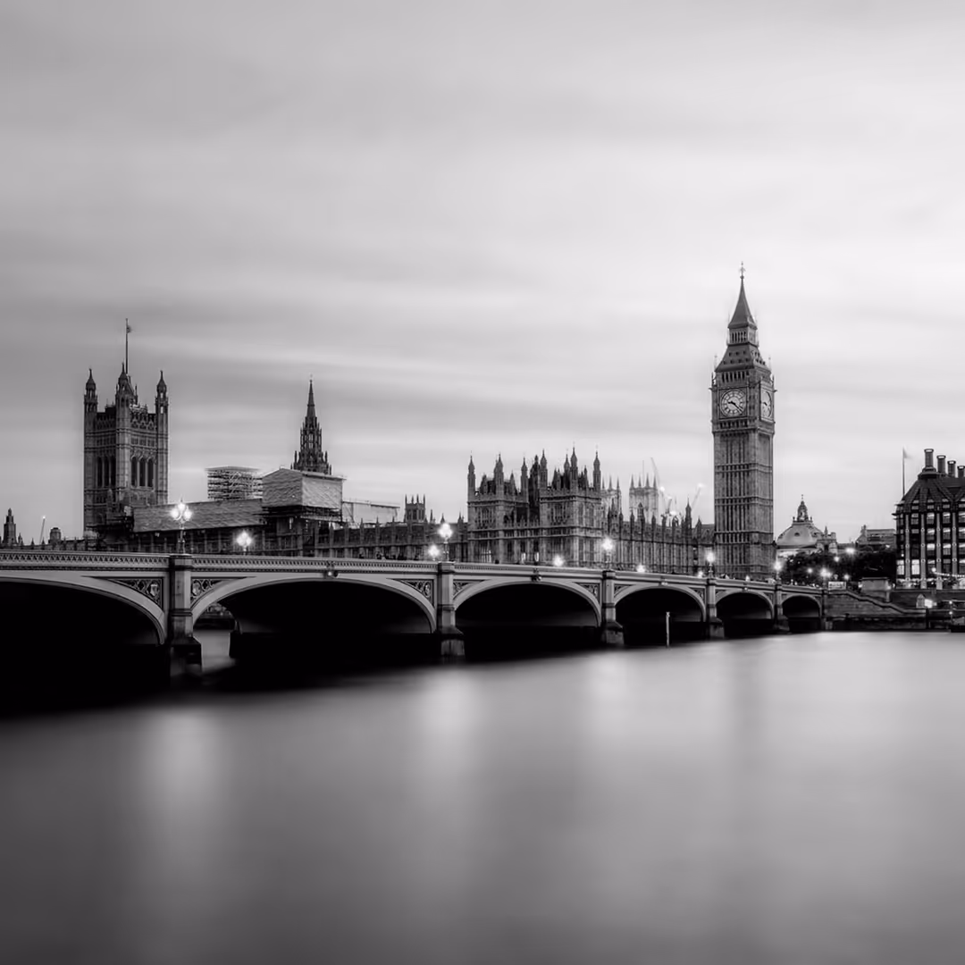 Black and white image of Westminster Palace and Big Ben at sunset, viewed across the River Thames.