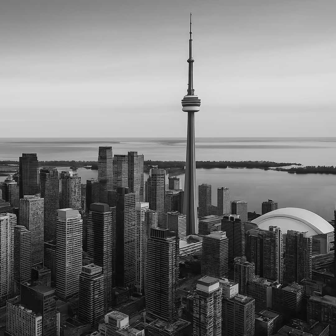 A black-and-white aerial view of downtown Toronto featuring the CN Tower, modern skyscrapers, and Lake Ontario in the background.