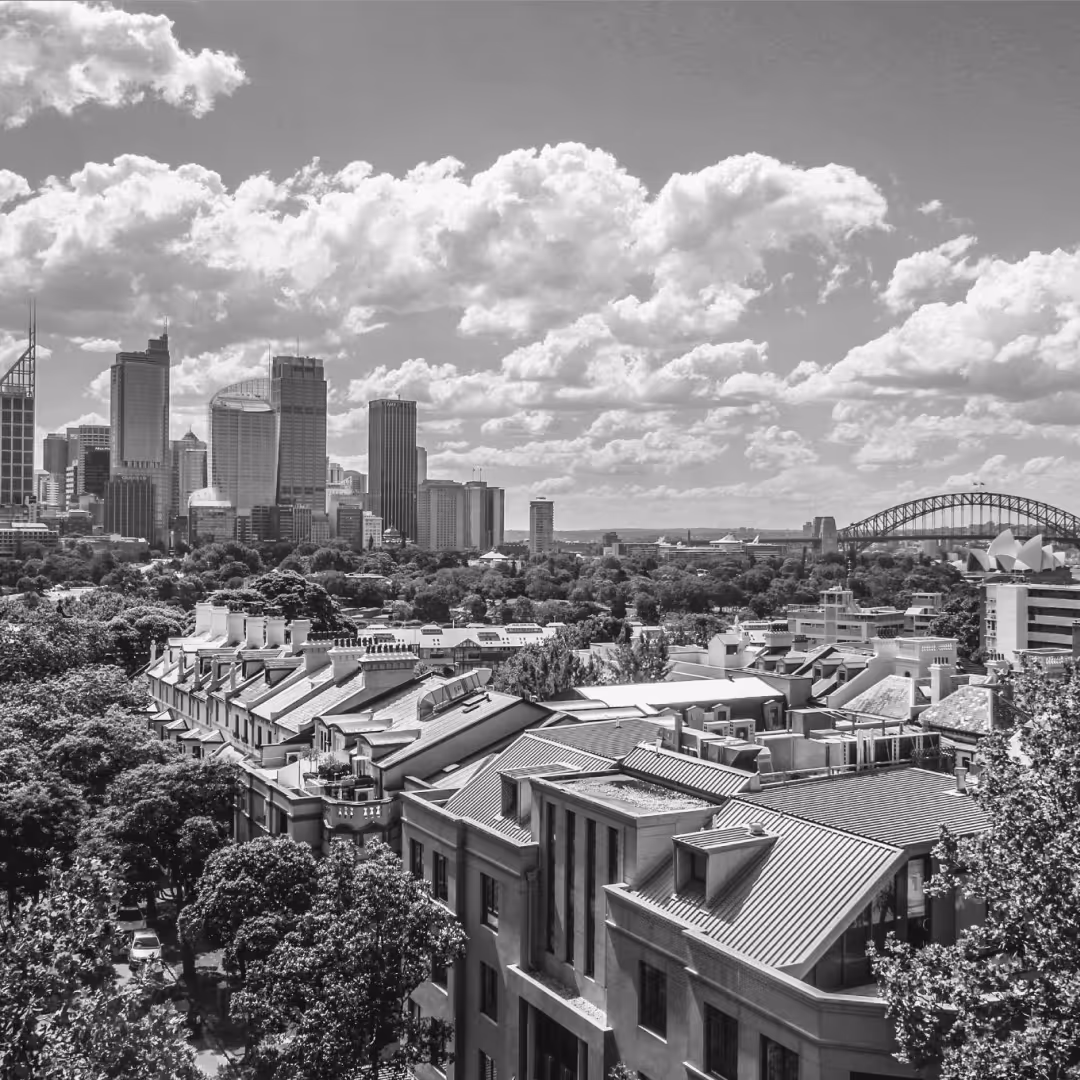 A daytime view of Sydney’s central business district with modern skyscrapers, lush greenery, and the Harbour Bridge visible in the distance.