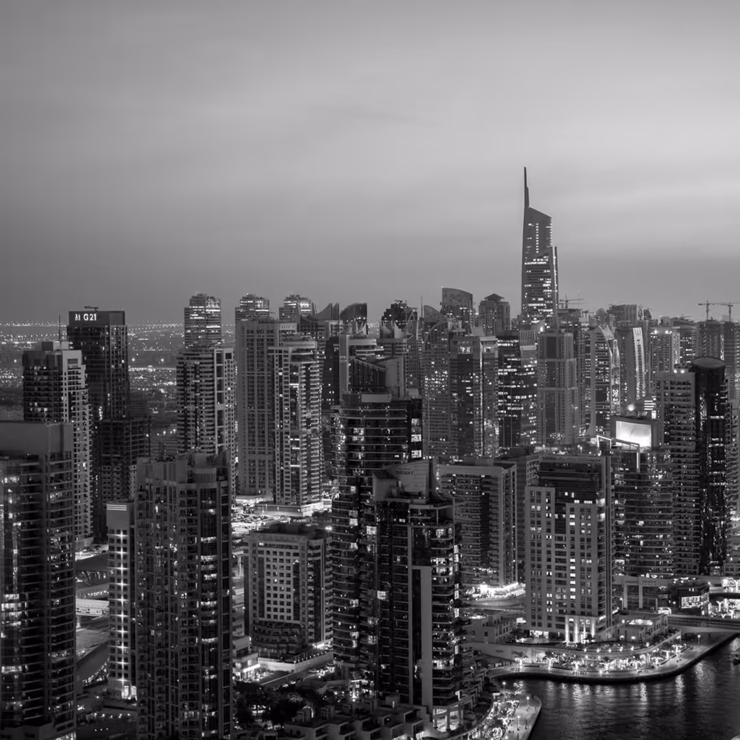 A panoramic view of Dubai’s illuminated skyscrapers, with modern high-rises clustered tightly together and lights reflecting off the marina below.