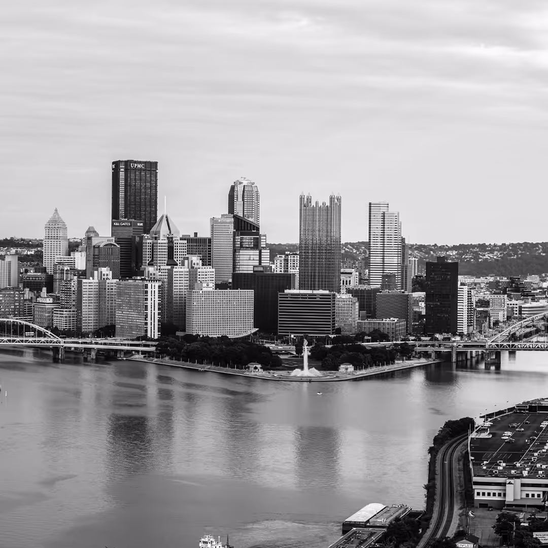 Aerial black-and-white view of Pittsburgh’s downtown with the fountain at Point State Park and multiple bridges crossing the rivers.