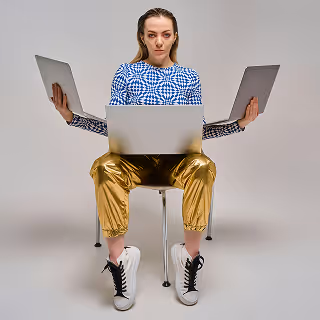 Woman sitting on a chair holding four laptops, symbolizing multitasking, productivity, and the demands of modern digital work culture.