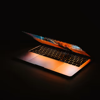 Half-closed laptop glowing in the dark with colorful screen reflections on the keyboard, creating a dramatic tech-focused ambiance.