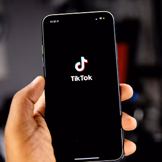 A hand holding a smartphone displaying the TikTok loading screen, highlighting content creation and mobile-first social engagement.