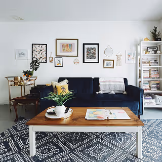 	Bright and eclectic living room featuring a navy couch, patterned rug, open bookshelf, and curated wall art gallery, conveying a vibrant and personalized hosting space.