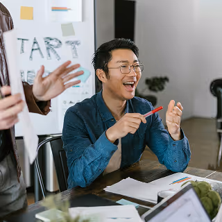 Young professional smiling and participating in a startup team meeting, with branding materials in the background, reflecting collaboration and fintech innovation.