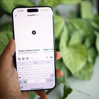 Hand holding a smartphone displaying the ChatGPT interface, with green leaves in soft focus background.