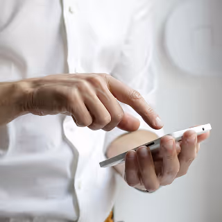 Close-up of a person in a white shirt using a smartphone with both hands, focused on the screen.