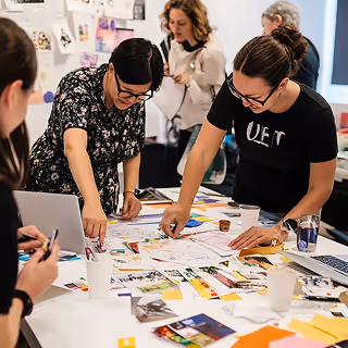 Creative professionals gather around a table covered with color swatches and printed materials, actively collaborating on a design or branding project.