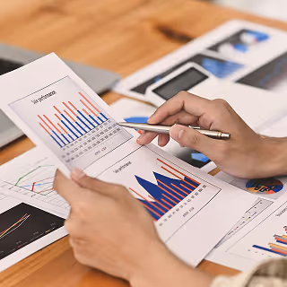 Close-up of hands reviewing printed marketing performance reports with colorful bar and line graphs on a wooden table.