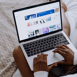 Hands on a laptop browsing a design website while sitting comfortably on a bed, representing casual yet productive creative work.
