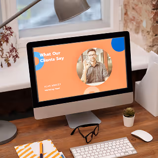 Desktop monitor showing a colorful testimonial slide with the title "What Our Clients Say" and a circular photo of a smiling man labeled "Alex Prince, Marketing Head," on a wooden desk.