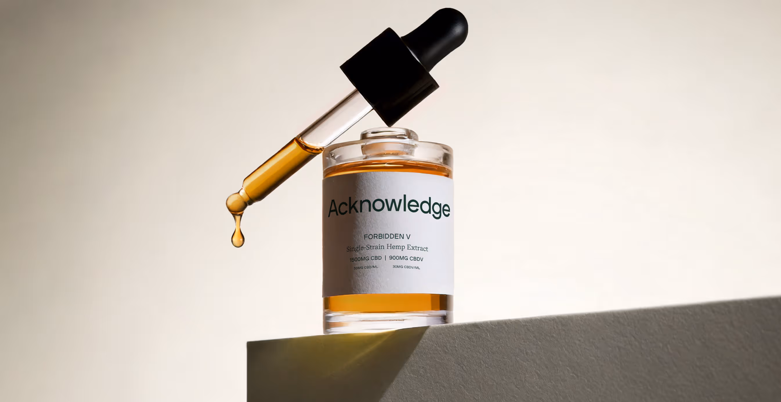 Acknowledge hemp extract bottle with a dropper releasing golden oil, captured against a light gradient background.