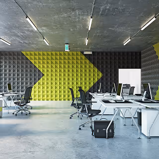 Modern office interior with open desk layout, black office chairs, and walls featuring black and yellow acoustic paneling in a geometric pattern.