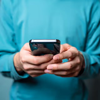 Close-up of a person in a teal shirt holding a smartphone with both hands, suggesting online shopping or mobile engagement.