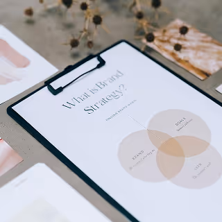 Clipboard with a brand strategy diagram featuring a Venn diagram – A neat branding workspace with a printed sheet titled "What is Brand Strategy?" and overlapping circles labeled brand, user, and goal.