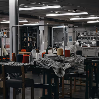 Interior of a textile manufacturing facility with striped fabric draped over machinery and spools of thread on workstations.
