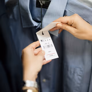 Close-up of a person holding a price tag on a blue collared shirt in a retail store.