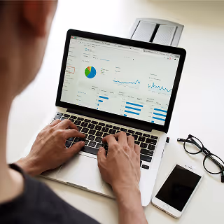 Close-up of a person using a laptop displaying graphs, pie charts, and metrics on a digital analytics dashboard.