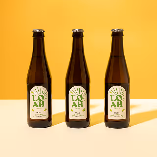 Three bottles of LOAH beer neatly aligned on a yellow and cream background, emphasizing minimalist branding and a modern aesthetic.
