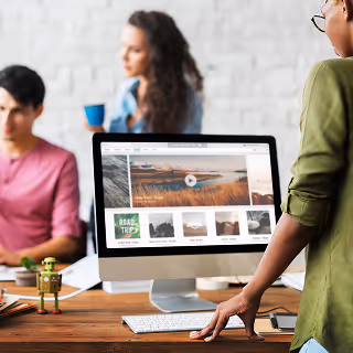 Creative professionals collaborating in an office space, with one person standing near a large monitor displaying a website design layout.