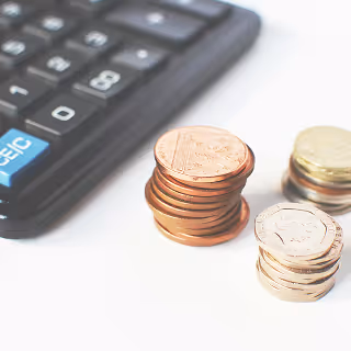 Close-up of stacked coins next to a black calculator on a white desk, representing budgeting or pricing considerations.