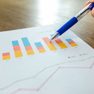 Close-up of a blue pen pointing at a colorful bar graph and line chart on a financial report.