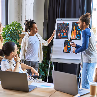 Diverse team of professionals discussing colorful analytics charts on a flip chart in a modern office setting.