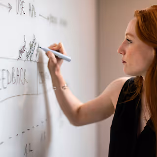 Focused red-haired woman writing keywords and strategy points on a whiteboard during a planning session.