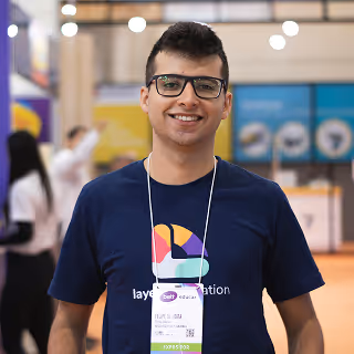 A smiling man wearing glasses and a tech conference badge, standing in a vibrant event space.