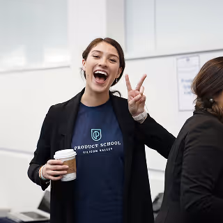 A cheerful woman flashing a peace sign and holding coffee at a tech event.
