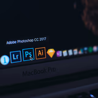Close-up of a MacBook Pro screen displaying Adobe Creative Cloud apps including Lightroom, Photoshop, and Illustrator.