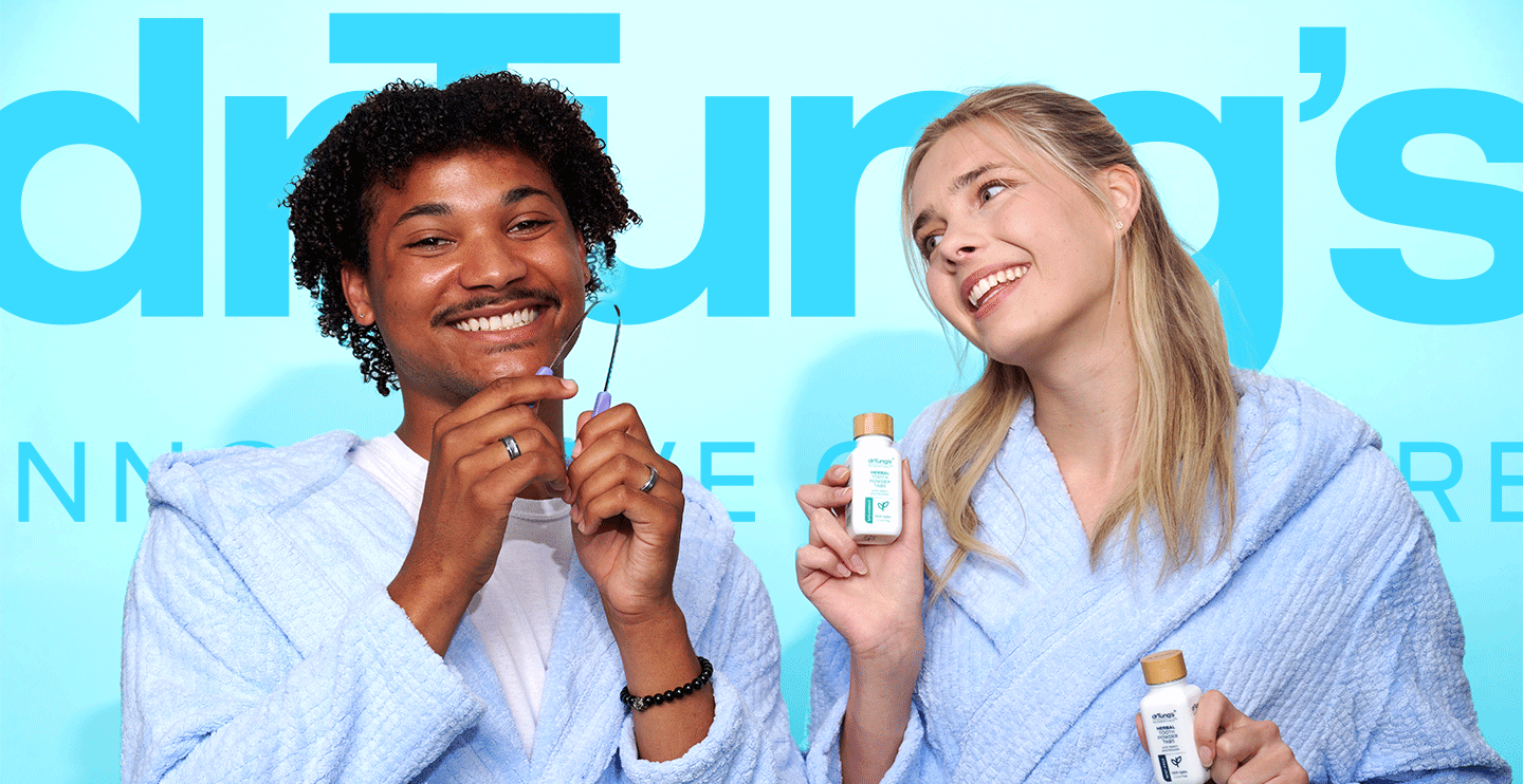 Two smiling models wearing light blue robes promote Dr. Tung’s oral care. One holds a purple tongue cleaner while the other shows a bottle of Herbal Toothpowder Tabs, set against a bright blue background with Dr. Tung’s branding.