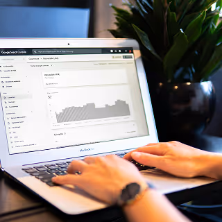 Close-up of hands typing on a MacBook Air displaying Google Search Console analytics, with a plant in the background.
