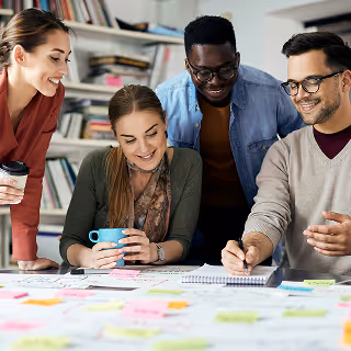 Creative team of four people brainstorming around a table covered in notes, sketches, and coffee mugs.