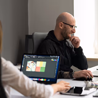 Male designer working at a computer in a modern office, with colorful graphic design software open on the screen.