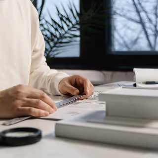 Close-up of hands arranging print materials and design tools on a desk with natural lighting, highlighting tactile elements of branding work.